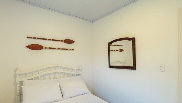 A bedroom with a bed, white bedding, a wooden headboard, two decorative paddles, and a mirror on the wall. - House With Pool and Barbecue in Itamambuca Cpi0130 (Ubatuba)