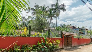 A residential area with a red wall, a wooden gate, and various tropical plants. - House With Pool and Barbecue in Itamambuca Cpi0130 (Ubatuba)