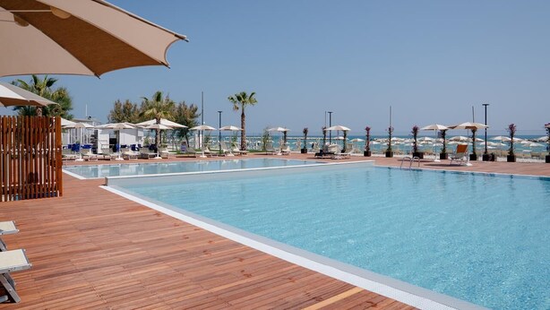 Un área de piscina con cubierta de madera, sillas de descanso y sombrillas.