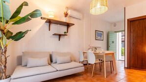 Una sala de estar acogedora con un sofá, una mesa de comedor con sillas, una lámpara colgante y una planta en maceta.