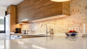 Una cucina moderna con mobili in legno, un piano di lavoro bianco, un lavello in acciaio inossidabile e uno schienale rivestito di piastrelle bianche.