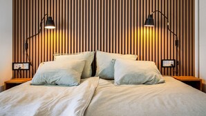 Camera da letto con parete in listelli di legno, due lampade da comodino, un letto con lenzuola a righe e un comodino con presa di corrente.