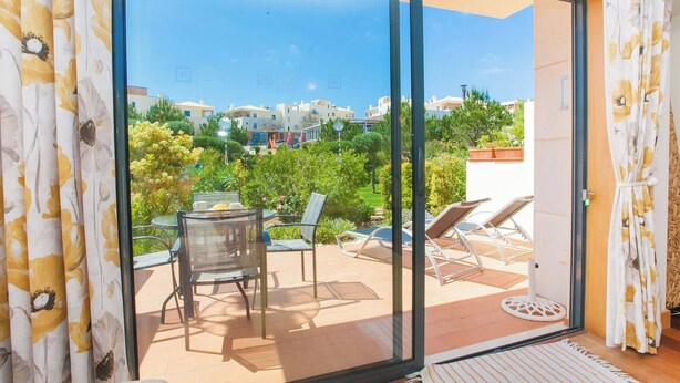 Un balcon doté d’une porte vitrée, de mobilier d’extérieur et offrant une vue sur des immeubles et des espaces verts.