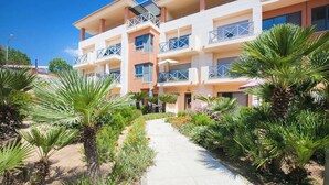Un immeuble à plusieurs étages doté de balcons, entouré de palmiers et bordé d’un sentier.