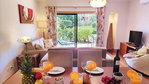 Un coin repas avec une table dressée pour quatre personnes, agrémentée de fruits, de vin et de pain.