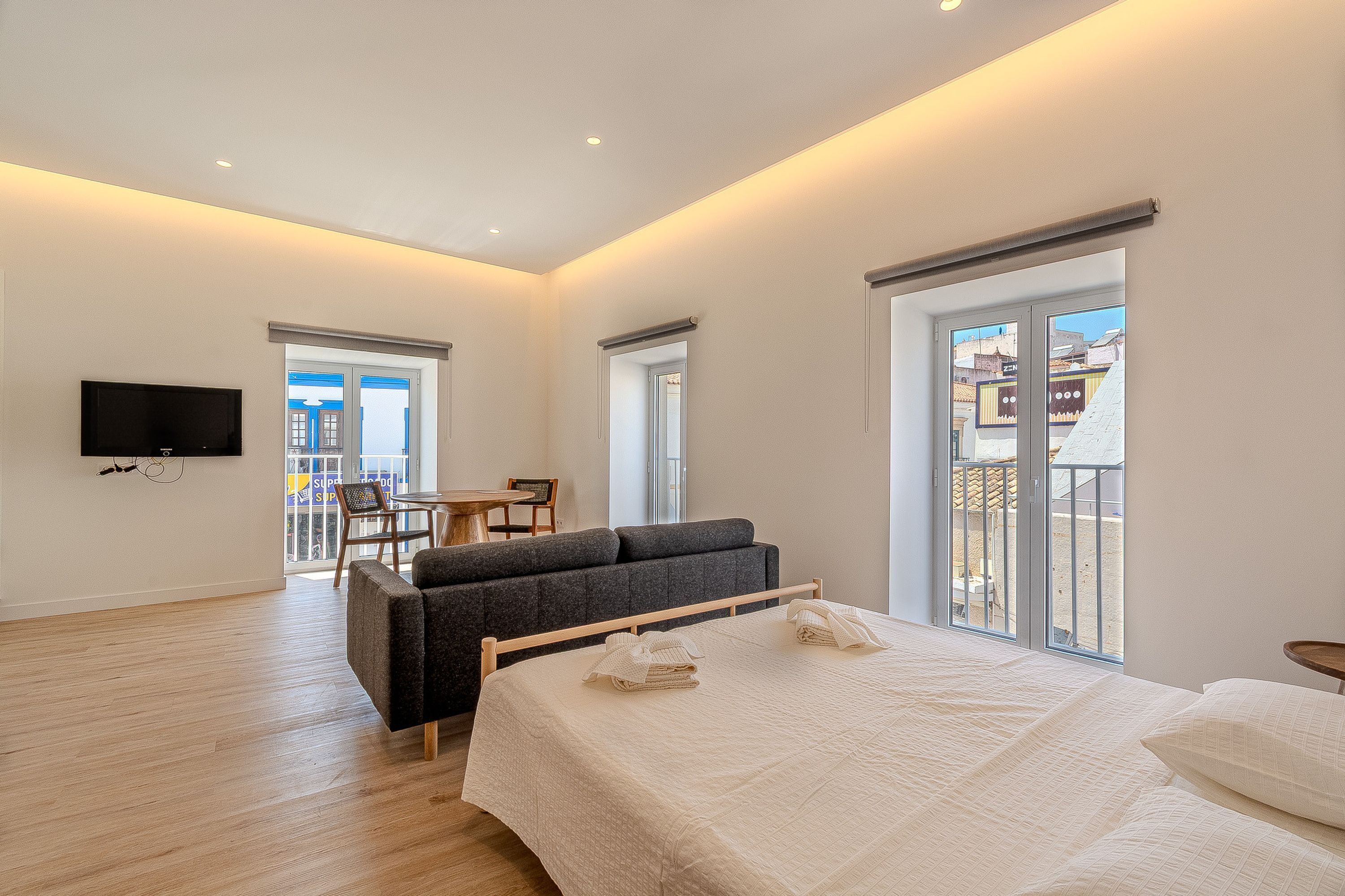 Una habitación de hotel moderna con una cama grande, un sofá, una televisión y un balcón con vistas a la ciudad.
