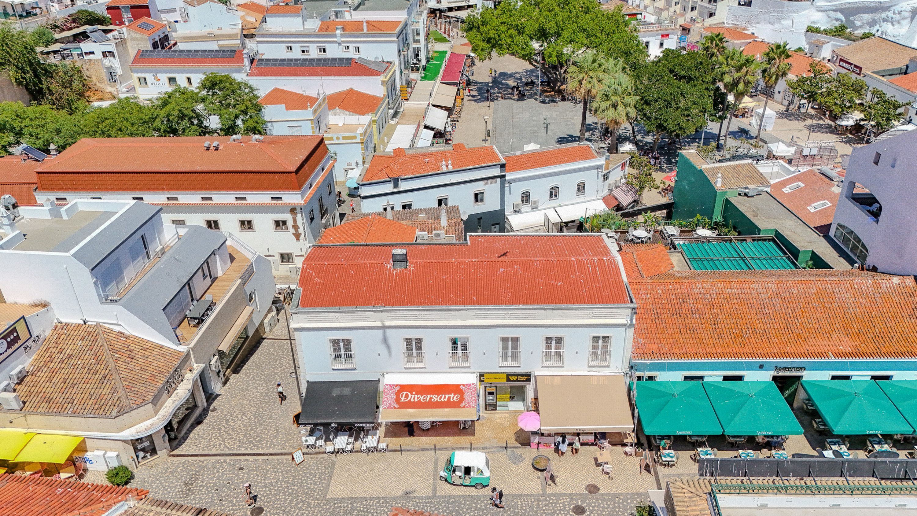 Vista a nivel de calle de un pueblo con edificios, un café y un vehículo pequeño.