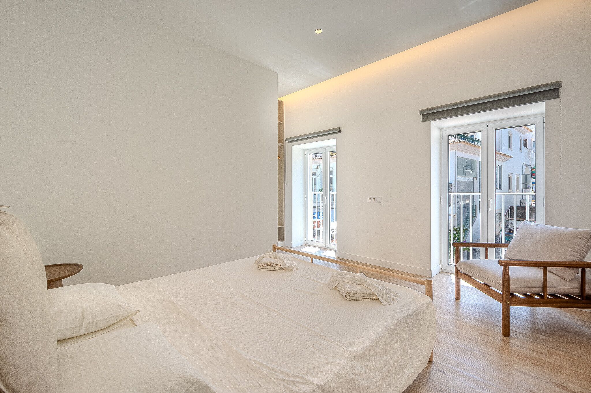 A bedroom with a large bed, a wooden chair, and a window with a view of buildings.