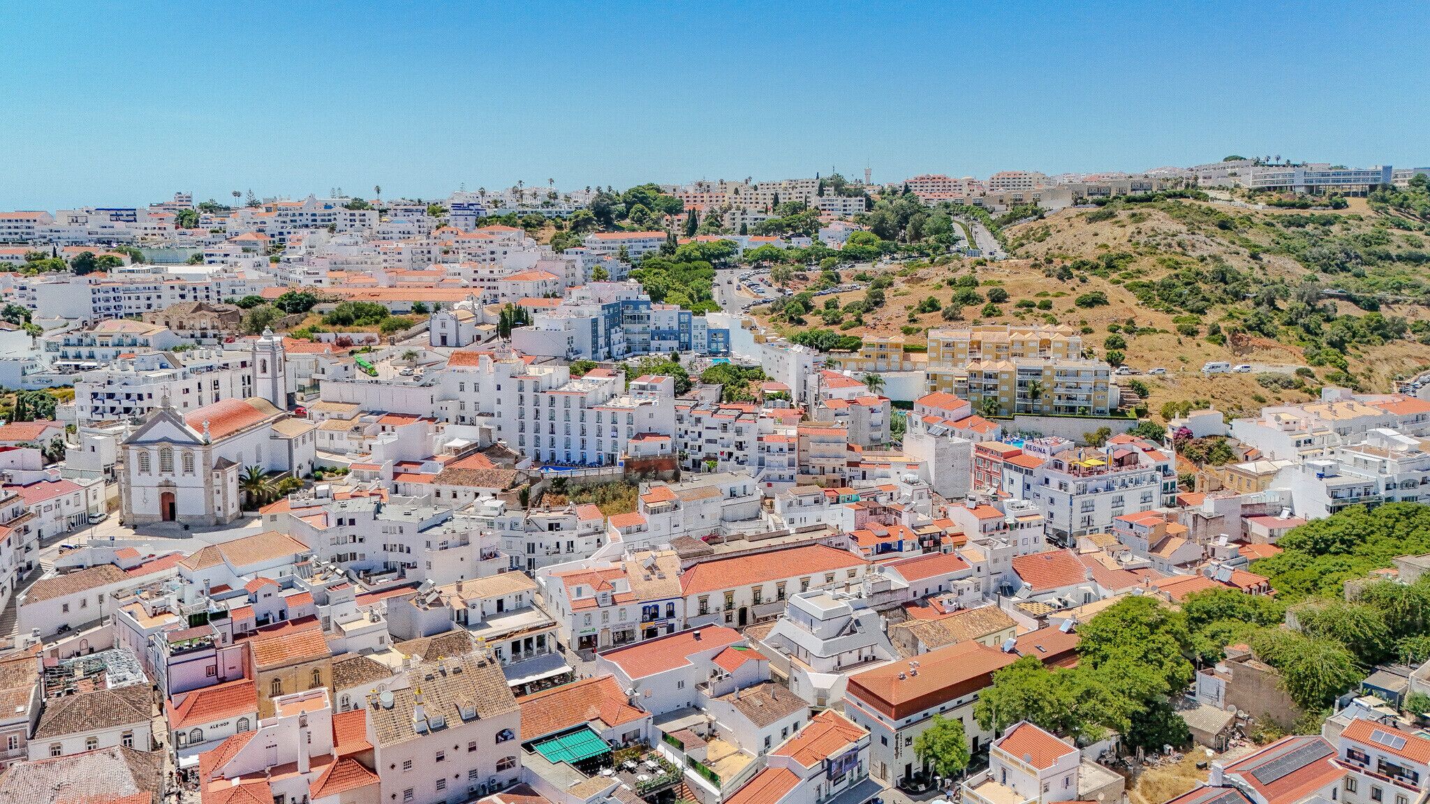 A densely packed urban area with a mix of residential and commercial buildings, featuring a prominent church and a hill with sparse vegetation.