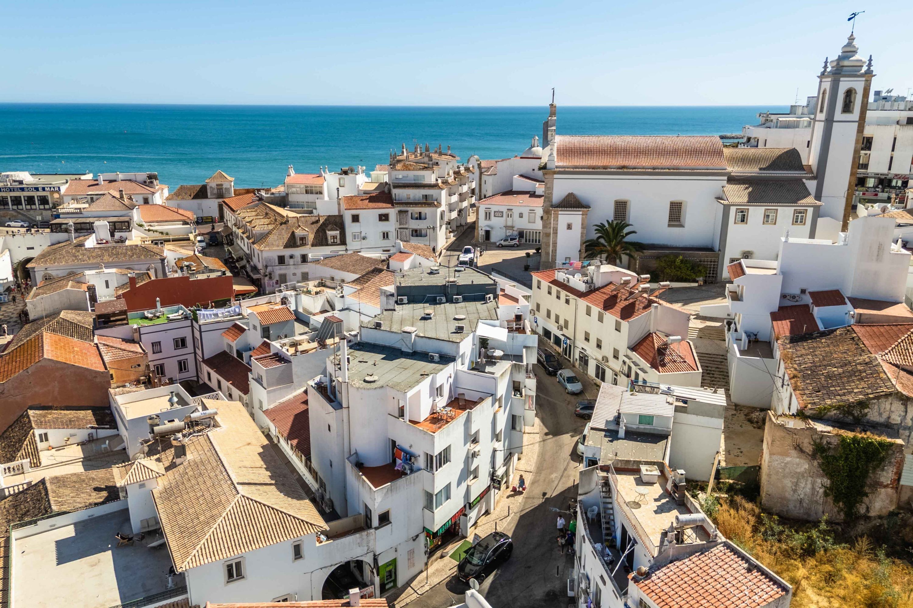 A coastal town with white buildings, a prominent church, and a clear view of the sea.