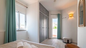 A hotel room with a bed, a wardrobe, a small stool, and a window with curtains. - Downtown Rooftop 1 Bedroom Apartment (Albufeira)
