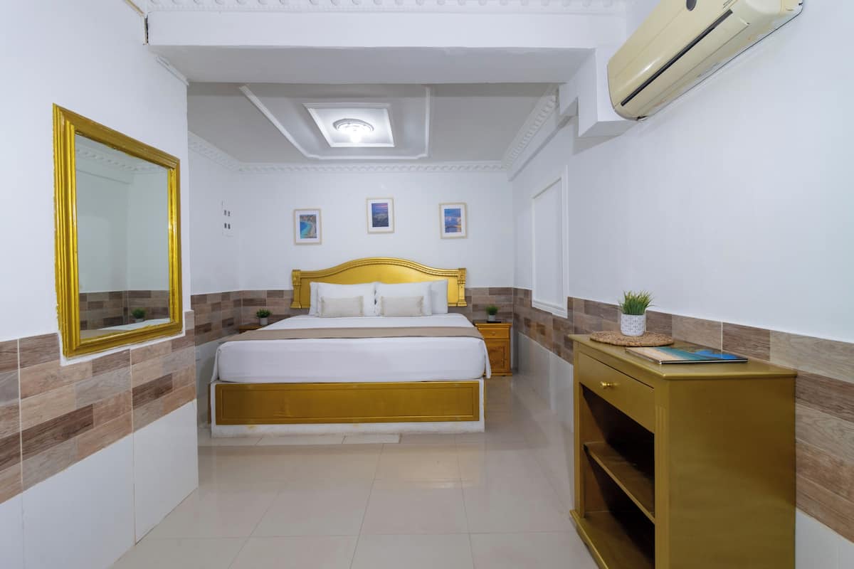 A bedroom with a bed, bedside tables, a mirror, and an air conditioning unit.