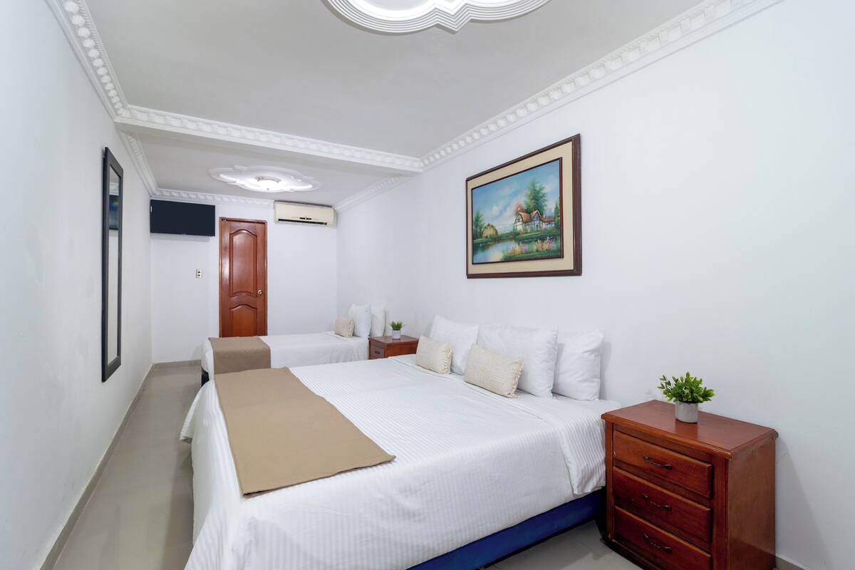 A bedroom with two beds, a wooden nightstand, a framed painting, and a small plant.