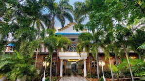 A hotel entrance with a tiled pathway leading to a covered area, surrounded by palm trees and potted plants. - Hotel Playa Salguero By GEH Suites  (Santa Marta)