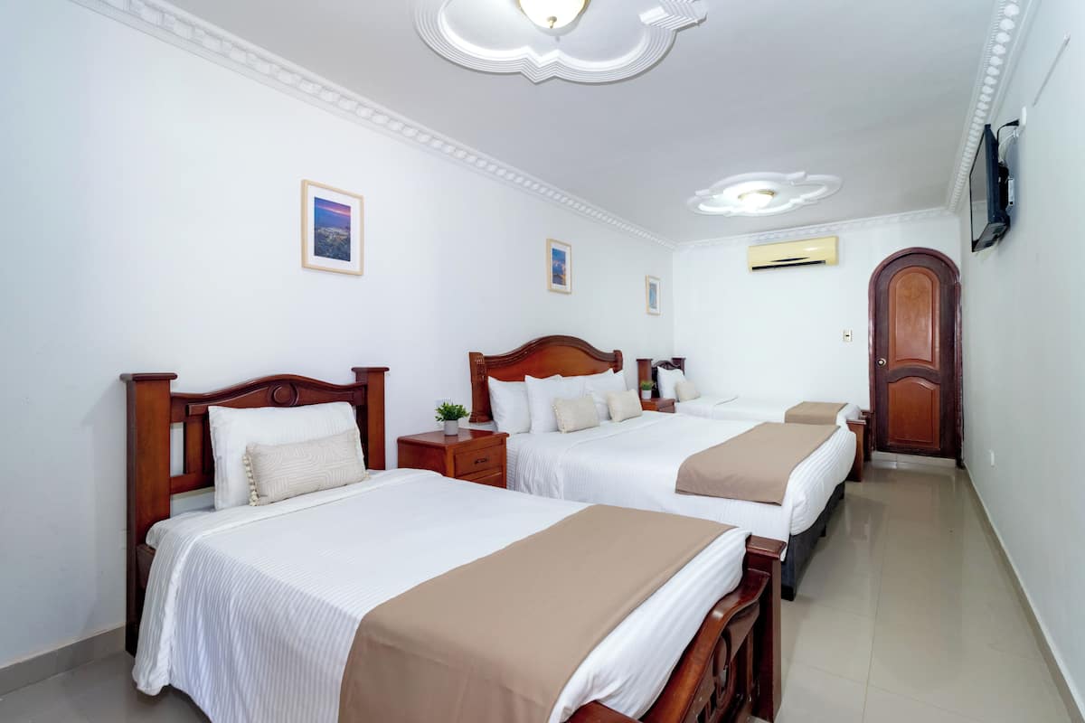A hotel room with two single beds, a wooden headboard, white bedding, a small bedside table with a lamp, and a TV mounted on the wall.