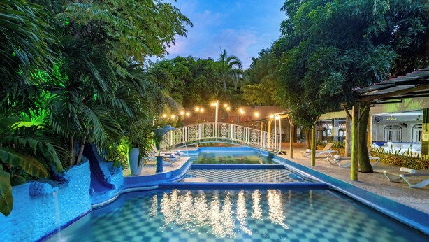 A pool with a checkered pattern, surrounded by lush greenery and a decorative bridge. - Hotel Playa Salguero By GEH Suites  (Santa Marta)