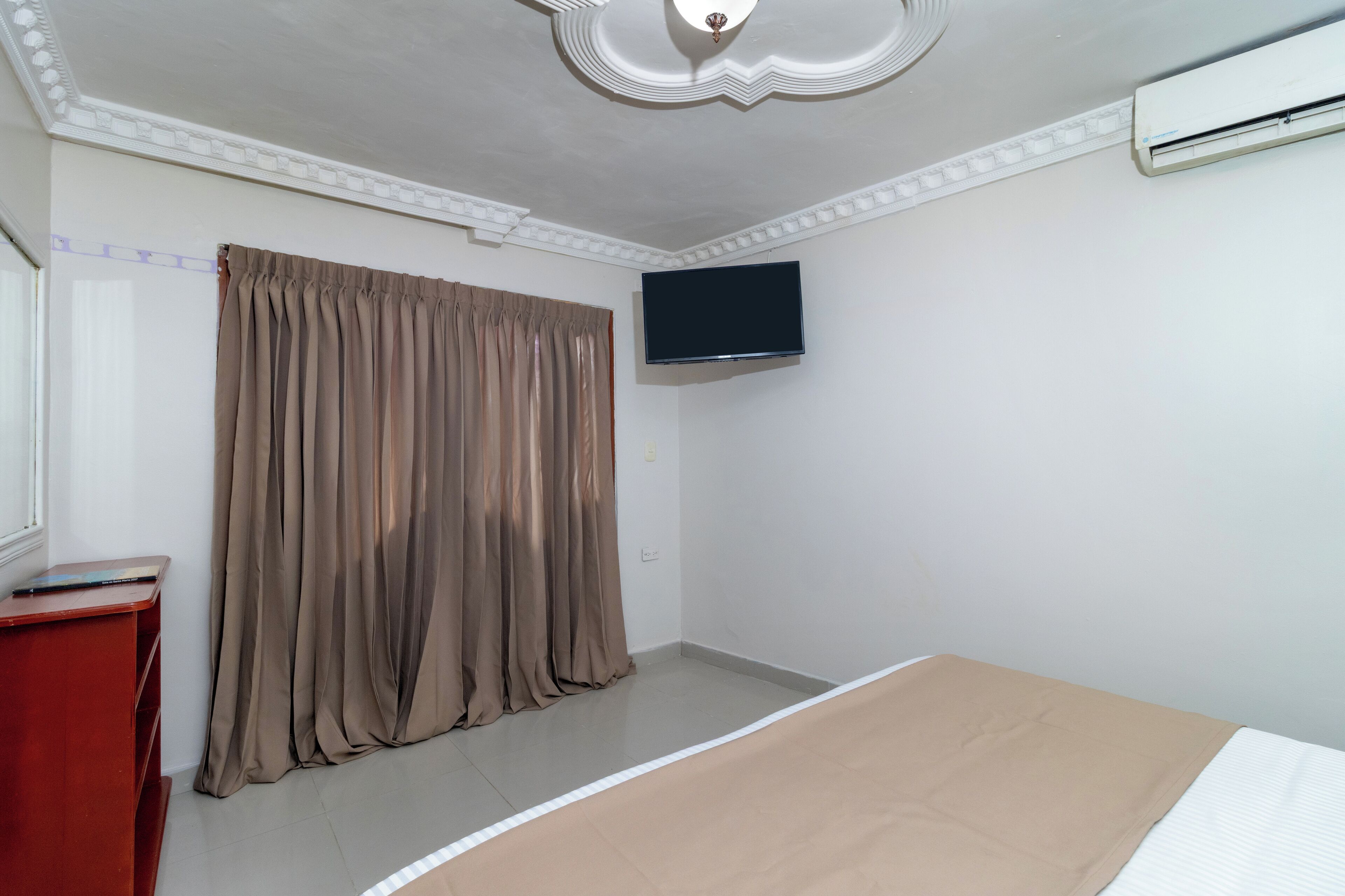 A hotel room with a bed, a TV mounted on the wall, and a curtain.