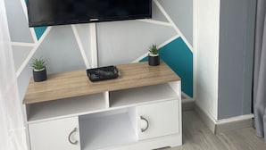 A modern living room with a flat-screen TV mounted on a wooden TV stand, two small potted plants, and a white cabinet with drawers.
