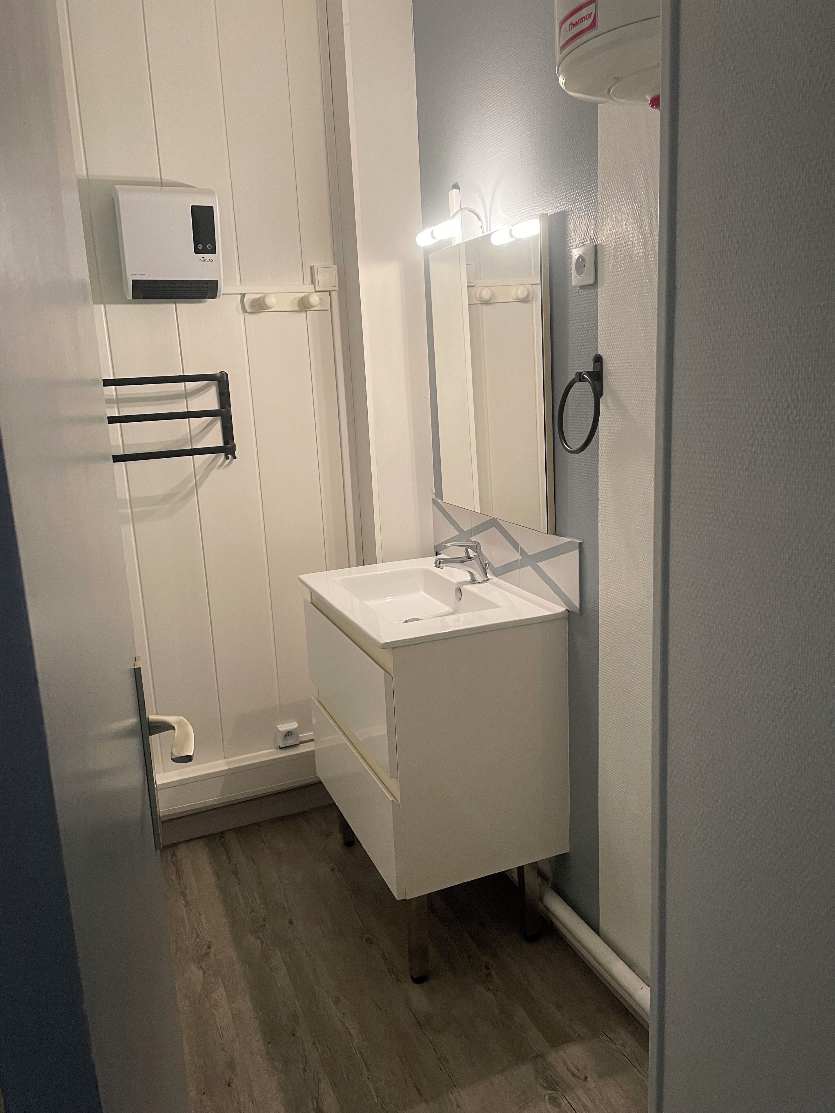 Une salle de bain avec un lavabo blanc, un miroir et un porte-serviettes.