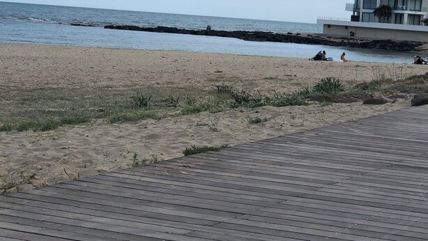 A beach with a wooden boardwalk, a rocky breakwater, and a modern building with balconies.
