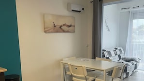 A modern living room with a dining table, chairs, a sofa, and a large window with a view.