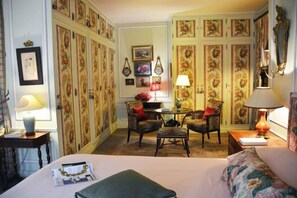 A hotel room with a bed, two armchairs, a small table, and a cabinet with floral wallpaper. - Elegant 3 Bedroom Apt Near Eiffel Tower - Alma (Paris)