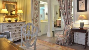 A room with a dining table, chairs, a sofa, a side table with a lamp, a mirror, and a floral-patterned chair. - Elegant 3 Bedroom Apt Near Eiffel Tower - Alma (Paris)