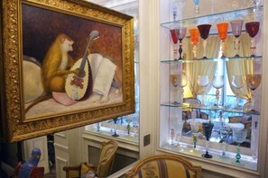 Une pièce comprenant un tableau encadré, une vitrine contenant divers objets en verre et un fauteuil.
