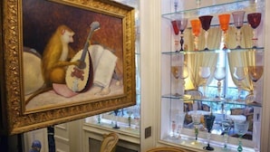 A room with a large framed painting of a monkey playing a flute, a glass display case with various glassware, and a window with curtains. - Elegant 3 Bedroom Apt Near Eiffel Tower - Alma (Paris)