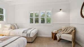 A bedroom with two beds, a chair, a small table, and a window with blinds. - Spencer House in Leura (Leura)
