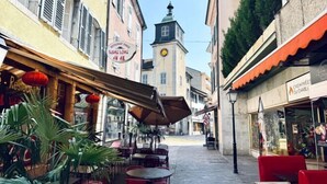 Une rue étroite avec des terrasses, un beffroi et diverses boutiques.