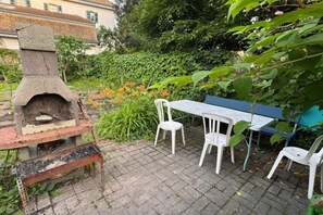 Une terrasse extérieure avec un four en pierre, des chaises blanches et une table.