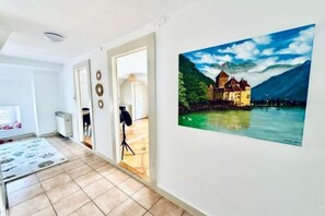 A room with a large painting of a castle by a lake, a door leading to another room, and a tripod in the corner. - Historic House Aigle - Lake & Alps - Garden & BBQ (Aigle)