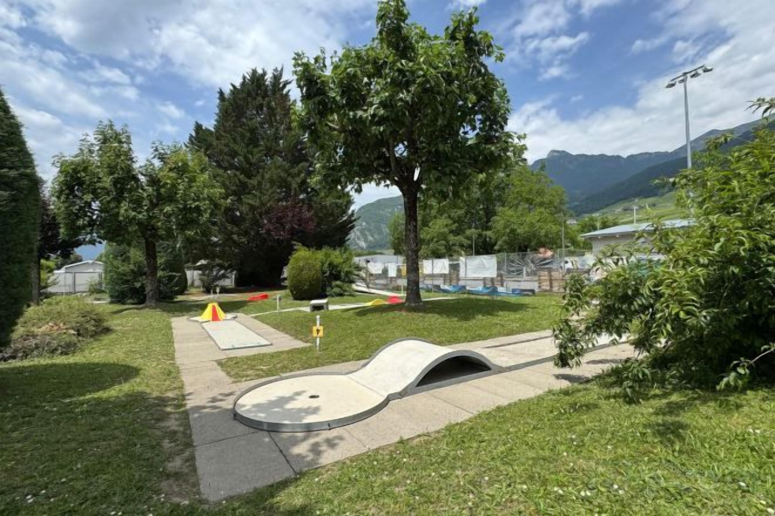 An outdoor area with a paved path, a small hill, and a tent.
