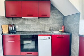 A compact kitchen with red cabinets, a dishwasher, an oven, and a sink. - Historic House Aigle - Lake & Alps - Garden & BBQ (Aigle)