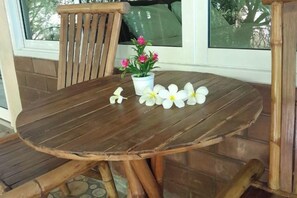 Une table ronde en bois, accompagnée d’une chaise, d’une plante en pot aux fleurs roses et de fleurs blanches posées sur la table.