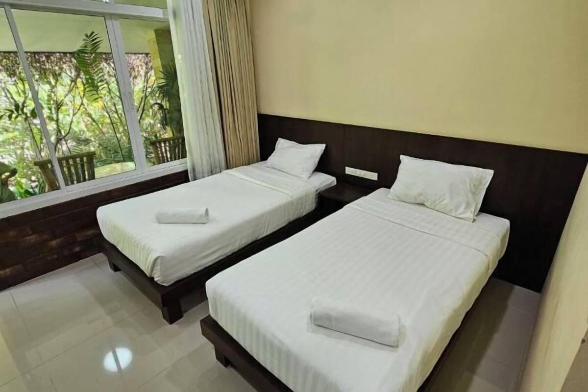 Two single beds with white linens and pillows, a wooden headboard, and a window with a view of greenery.