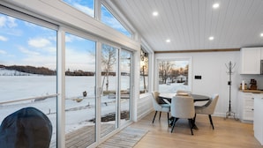 A modern kitchen with large windows, a dining area, and a view of a snowy landscape. - Cottage Retreat (Paroisse de Sainte-Marie)