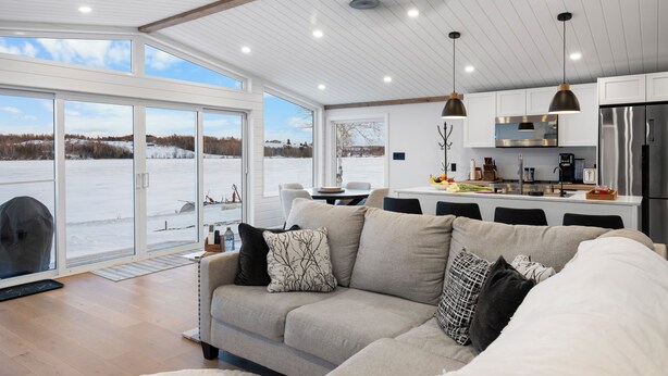 Ett modernt kök med ett kylskåp i rostfritt stål, en matplats med bord och stolar samt ett stort fönster med utsikt över ett snötäckt landskap.