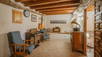 A room with a wooden ceiling, a piano, a guitar, a radio, and a bed with a patterned bedspread.