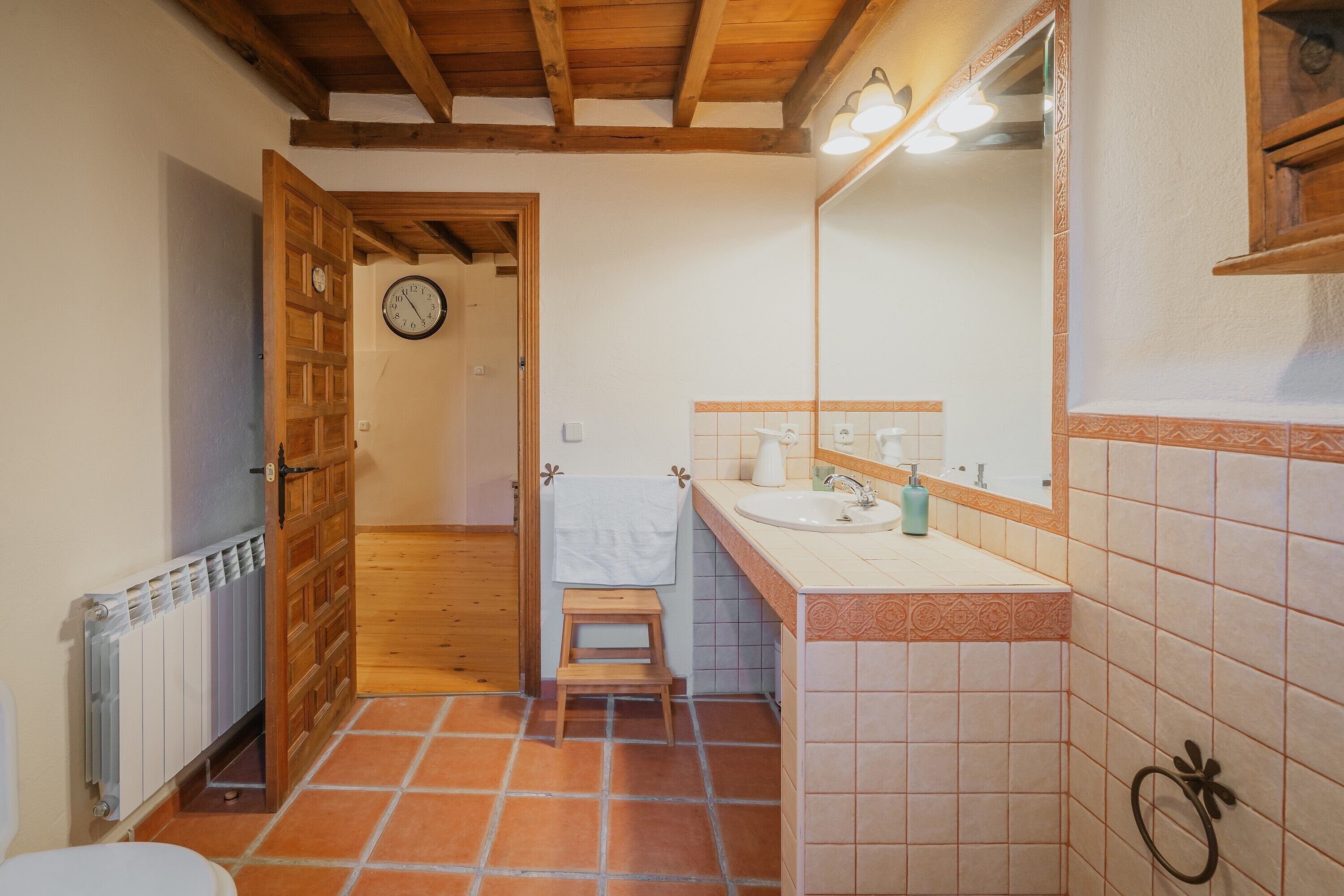 Une salle de bain avec une porte en bois, un lavabo blanc, un miroir et un sol carrelé.