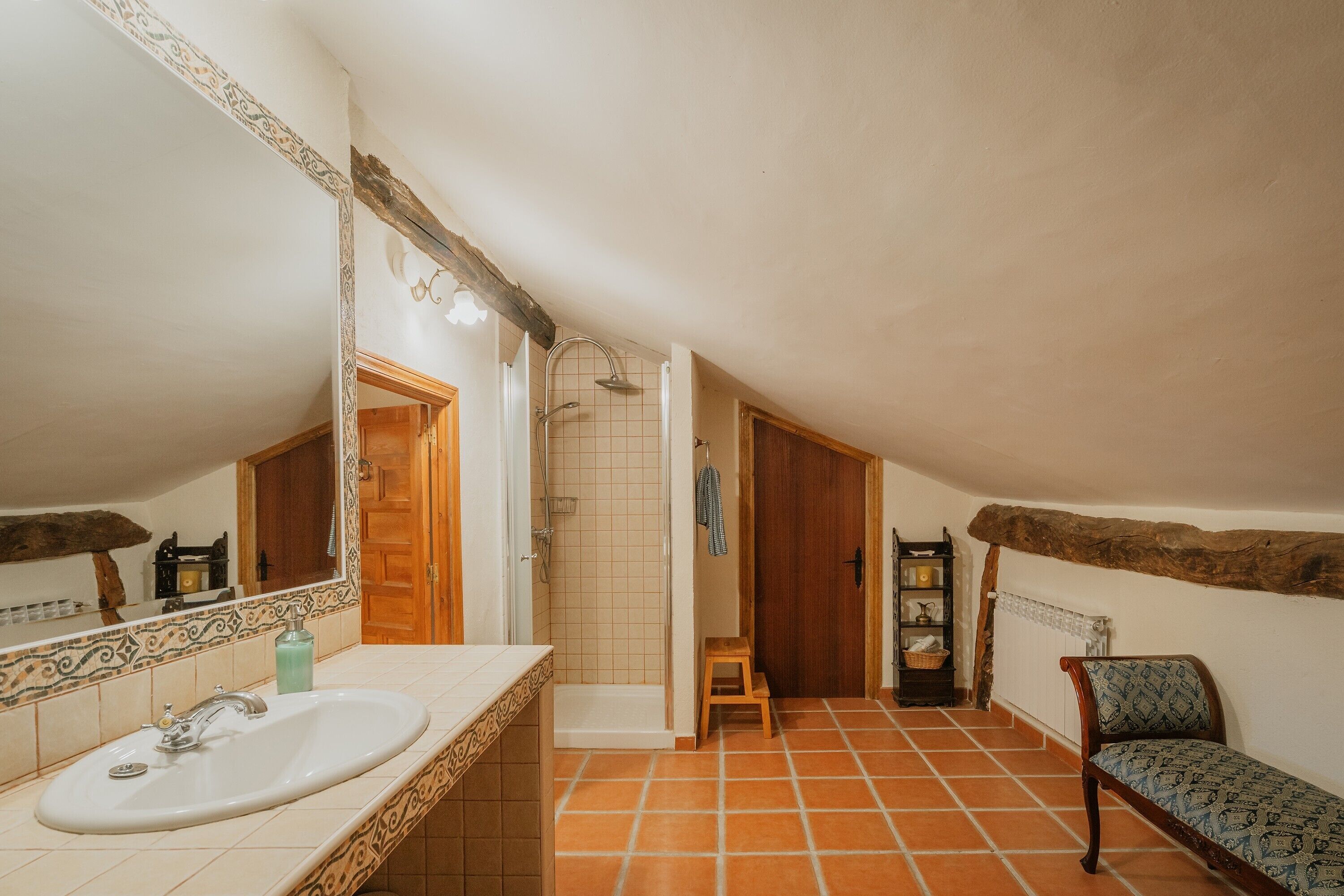 A bathroom with a sink, shower, and a bench.