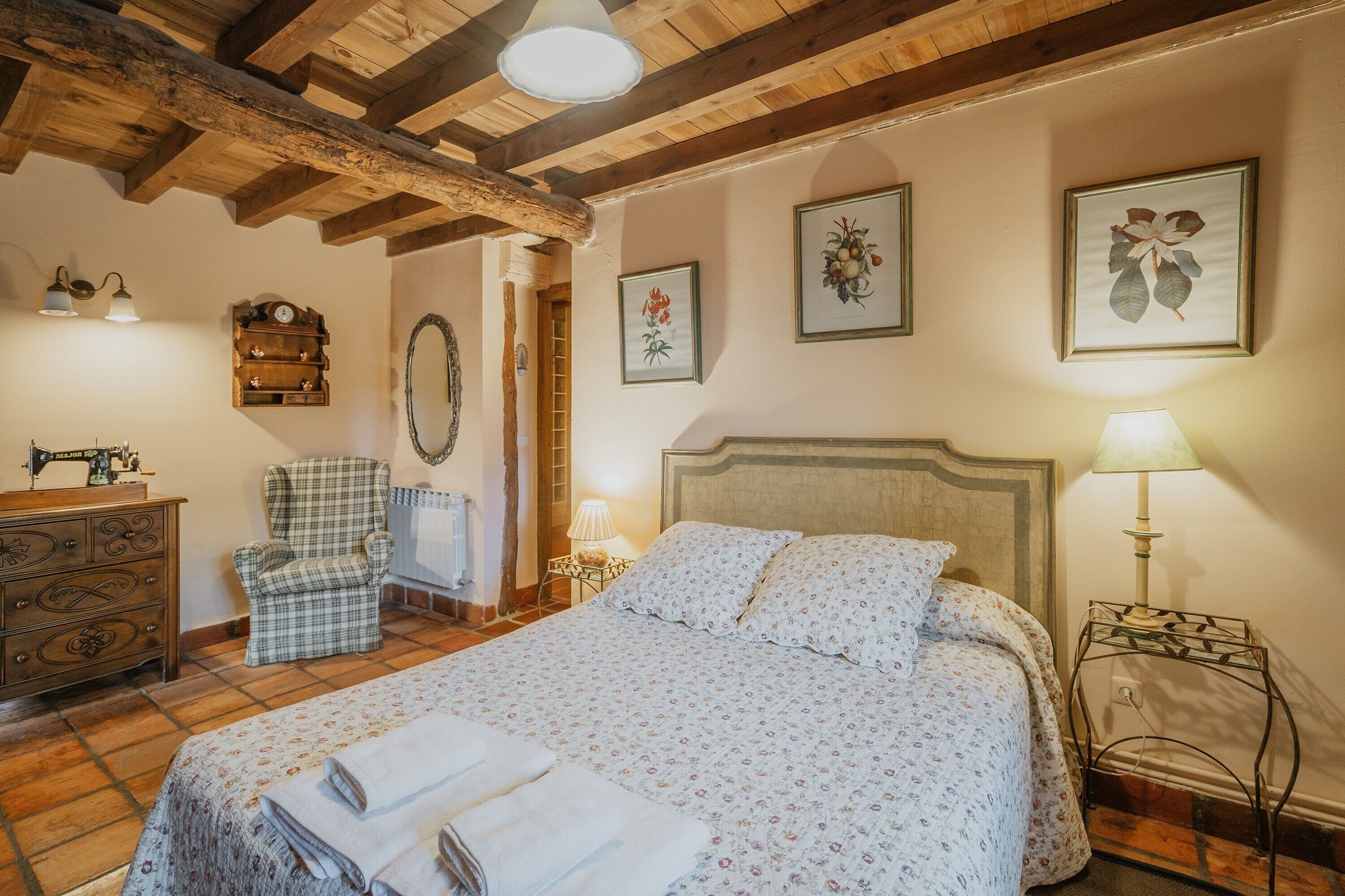 A bedroom with a bed, dresser, chair, and wall-mounted lamp.