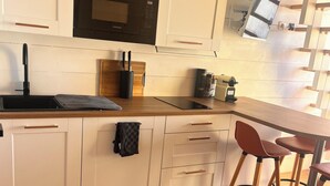 A modern kitchen with white cabinetry, a black microwave, and a wooden countertop. There are two stools and a small table. - A nugget with a 180° view of the ocean and its splendid sunsets. (Lacanau)