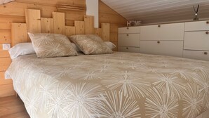 A bedroom with a wooden headboard, a bed with a beige floral-patterned bedspread, and white storage units with round knobs. - A nugget with a 180° view of the ocean and its splendid sunsets. (Lacanau)