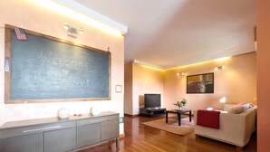 Una sala de estar moderna con una pizarra grande que muestra "WELCOME BENJENUT!", un televisor, un sofá, una mesa de centro y un mueble.