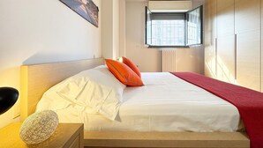 Una cama bien hecha con ropa de cama blanca y roja, un cabecero de madera y un adorno en la mesita de noche.