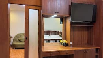 Una stanza con una scrivania in legno, uno specchio, una televisione e un letto con un divano verde sullo sfondo.