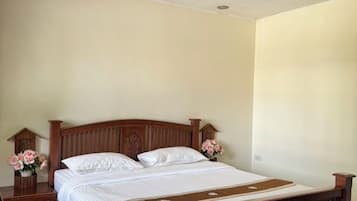 A single bed with a wooden headboard, two bedside tables, and a nightstand with a vase of flowers.