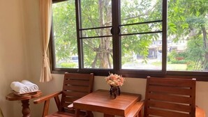 A room with a wooden table and chairs, a window with a view of trees, and a vase with flowers. - Rommaiplaitawan hotel & resort (Nakhon Ratchasima)